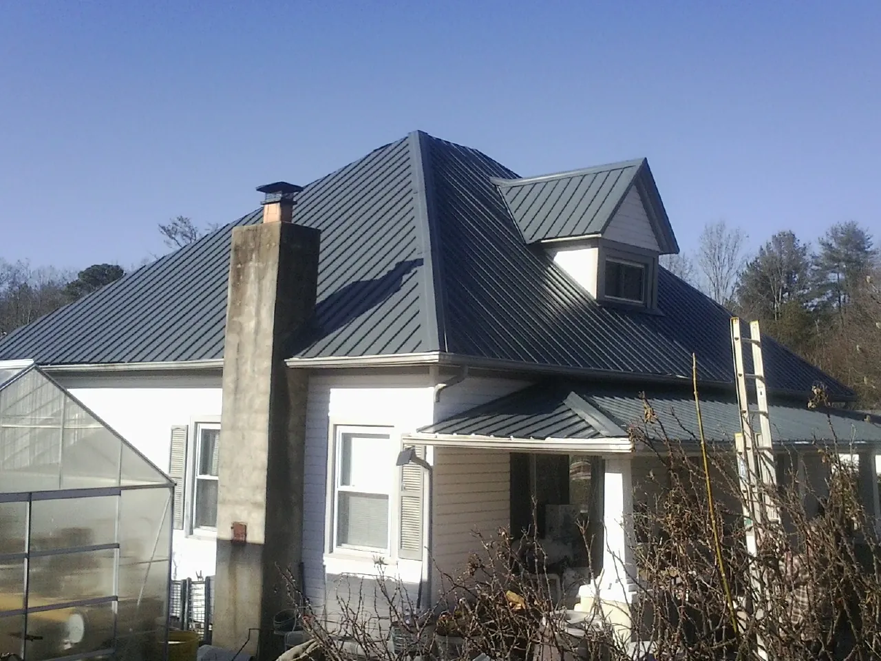 Dark blue standing seam metal roof on a white farmhouse with dormer — Slate & Tile Roof Repair by Roofing Brothers in Goodview