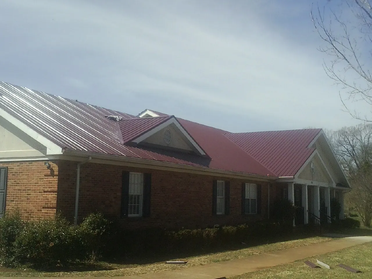 Red metal roof with gabled entries on a long brick building, from a Hail Damage Roof Repair job in Goodview