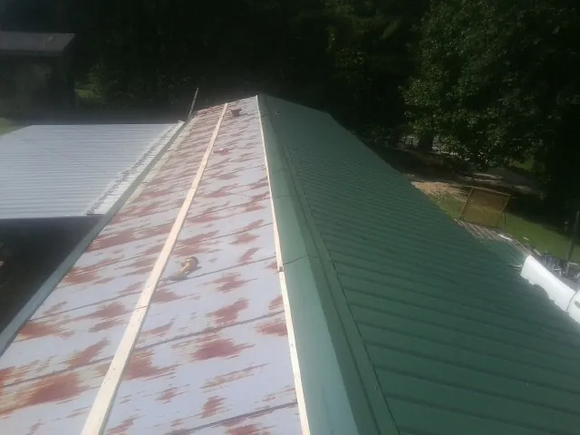 Old rusted panels beside newly installed green metal roofing — Wind Damage Roof Repair by Roofing Brothers in Goodview