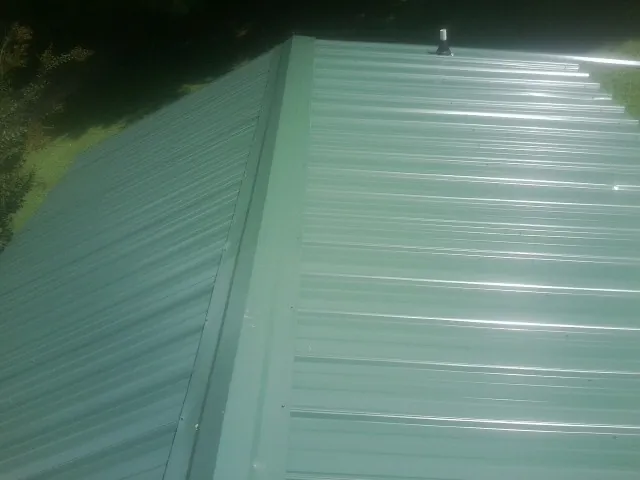New green metal panels meeting at the ridge of a roof — Flat Roof Repair work by our crew in Goodview